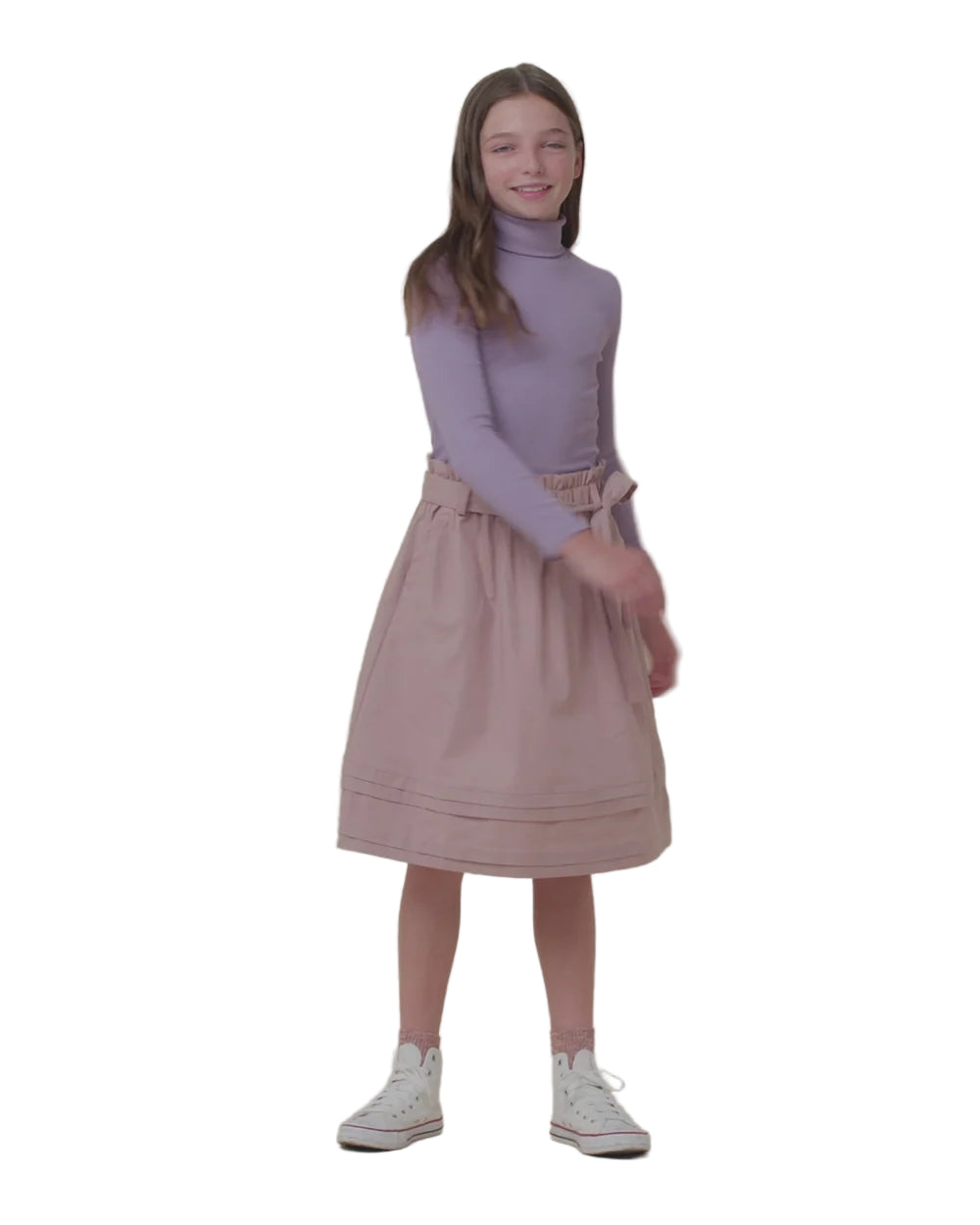 Young girl wearing a purple turtleneck and pink skirt against a beige background